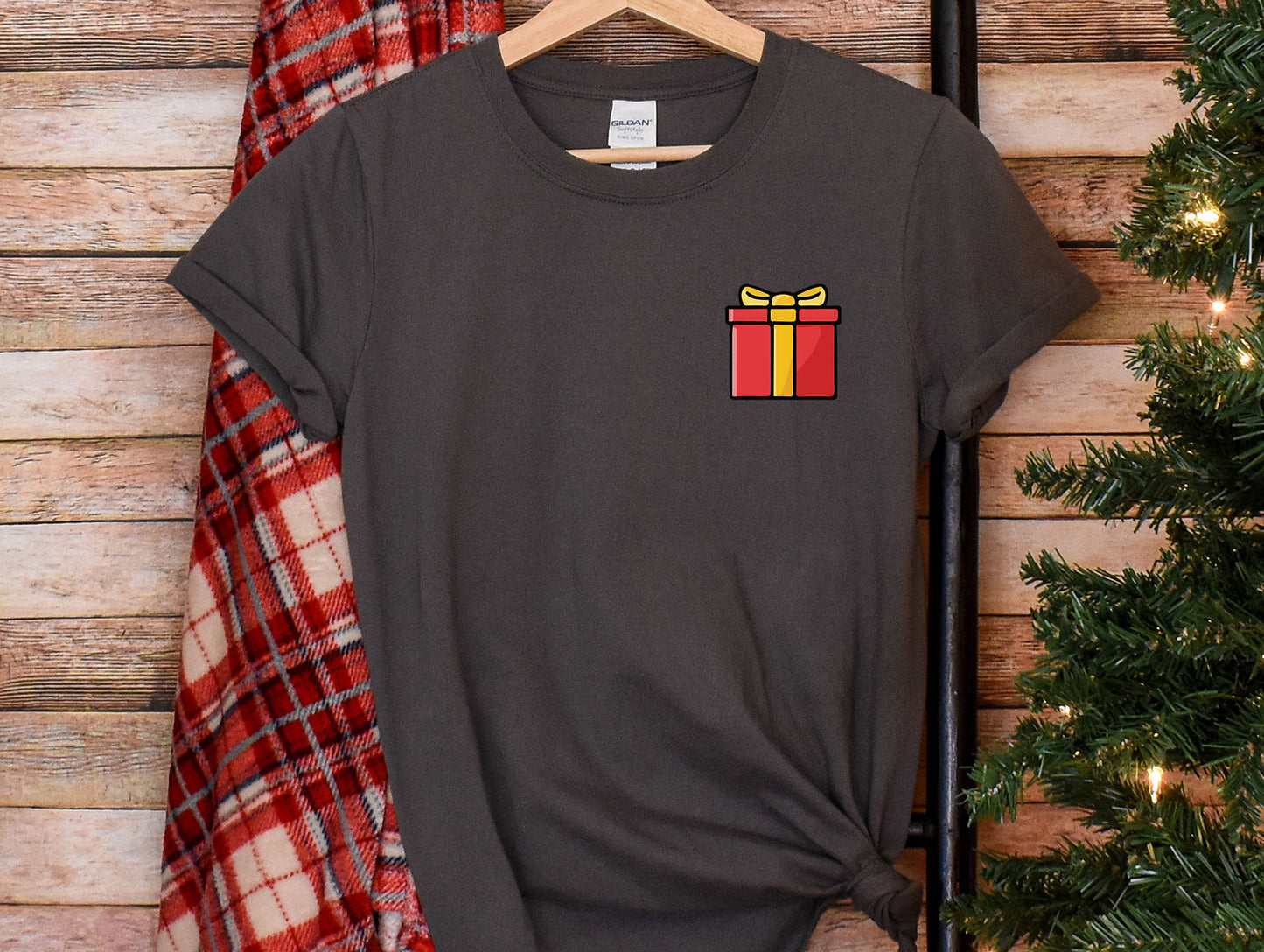 a t - shirt with a gift box on it hanging next to a christmas tree